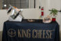 King Cheese table cloth draped over a table with cheese cutter on it.