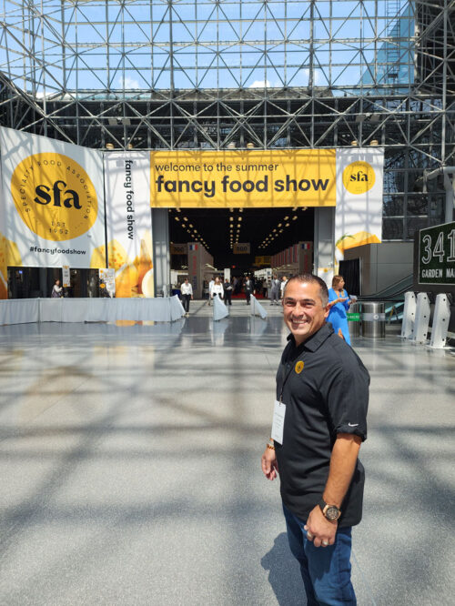 Vicken Aghchikian standing outside in front of a banner for Fancy food Show.